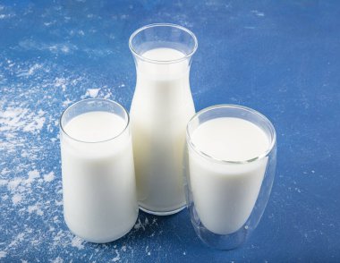 Temiz kavanozlardaki saf süt içecekleri ve şişeler mavi arka planda doğal olarak sağlıklı gıdalardır. Bir şişe süt ve bir bardak süt mavi arka plandaki ahşap bir masada.. 