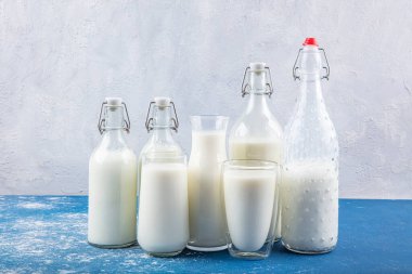 Temiz kavanozlardaki saf süt içecekleri ve şişeler mavi arka planda doğal olarak sağlıklı gıdalardır. Bir şişe süt ve bir bardak süt mavi arka plandaki ahşap bir masada.. 