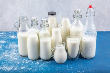 Temiz kavanozlardaki saf süt içecekleri ve şişeler mavi arka planda doğal olarak sağlıklı gıdalardır. Bir şişe süt ve bir bardak süt mavi arka plandaki ahşap bir masada.. 