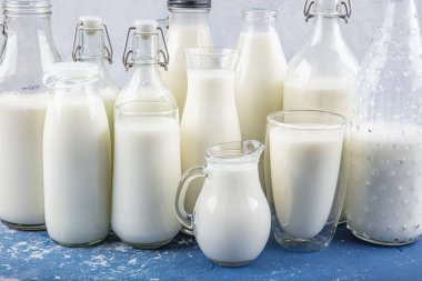 Temiz kavanozlardaki saf süt içecekleri ve şişeler mavi arka planda doğal olarak sağlıklı gıdalardır. Bir şişe süt ve bir bardak süt mavi arka plandaki ahşap bir masada.. 