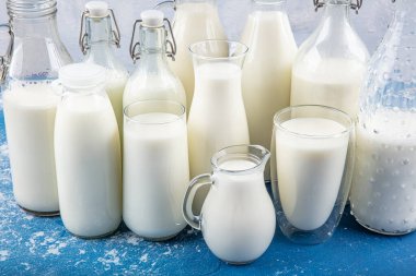 Temiz kavanozlardaki saf süt içecekleri ve şişeler mavi arka planda doğal olarak sağlıklı gıdalardır. Bir şişe süt ve bir bardak süt mavi arka plandaki ahşap bir masada.. 