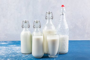 Temiz kavanozlardaki saf süt içecekleri ve şişeler mavi arka planda doğal olarak sağlıklı gıdalardır. Bir şişe süt ve bir bardak süt mavi arka plandaki ahşap bir masada.. 