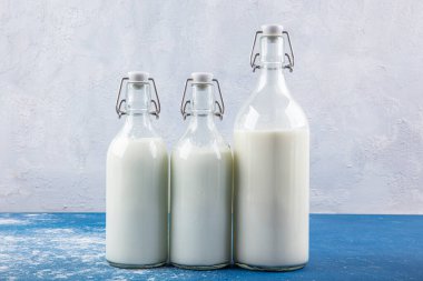 Temiz kavanozlardaki saf süt içecekleri ve şişeler mavi arka planda doğal olarak sağlıklı gıdalardır. Bir şişe süt ve bir bardak süt mavi arka plandaki ahşap bir masada.. 