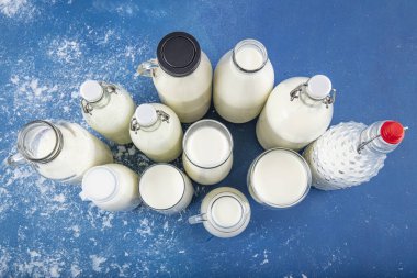 Temiz kavanozlardaki saf süt içecekleri ve şişeler mavi arka planda doğal olarak sağlıklı gıdalardır. Bir şişe süt ve bir bardak süt mavi arka plandaki ahşap bir masada.. 