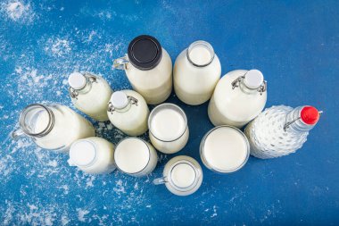 Temiz kavanozlardaki saf süt içecekleri ve şişeler mavi arka planda doğal olarak sağlıklı gıdalardır. Bir şişe süt ve bir bardak süt mavi arka plandaki ahşap bir masada.. 