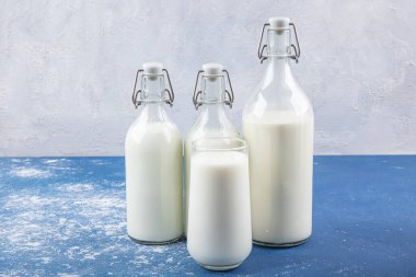 Temiz kavanozlardaki saf süt içecekleri ve şişeler mavi arka planda doğal olarak sağlıklı gıdalardır. Bir şişe süt ve bir bardak süt mavi arka plandaki ahşap bir masada.. 