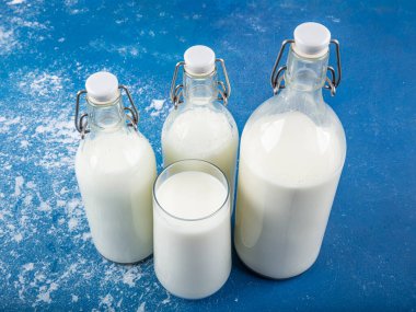 Temiz kavanozlardaki saf süt içecekleri ve şişeler mavi arka planda doğal olarak sağlıklı gıdalardır. Bir şişe süt ve bir bardak süt mavi arka plandaki ahşap bir masada.. 