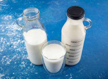 Temiz kavanozlardaki saf süt içecekleri ve şişeler mavi arka planda doğal olarak sağlıklı gıdalardır. Bir şişe süt ve bir bardak süt mavi arka plandaki ahşap bir masada.. 