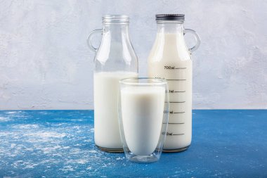 Temiz kavanozlardaki saf süt içecekleri ve şişeler mavi arka planda doğal olarak sağlıklı gıdalardır. Bir şişe süt ve bir bardak süt mavi arka plandaki ahşap bir masada.. 