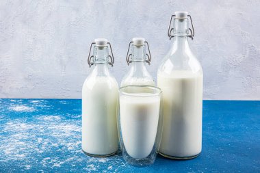 Temiz kavanozlardaki saf süt içecekleri ve şişeler mavi arka planda doğal olarak sağlıklı gıdalardır. Bir şişe süt ve bir bardak süt mavi arka plandaki ahşap bir masada.. 