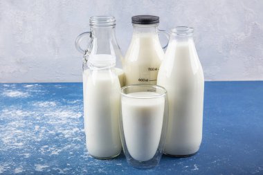 Temiz kavanozlardaki saf süt içecekleri ve şişeler mavi arka planda doğal olarak sağlıklı gıdalardır. Bir şişe süt ve bir bardak süt mavi arka plandaki ahşap bir masada.. 