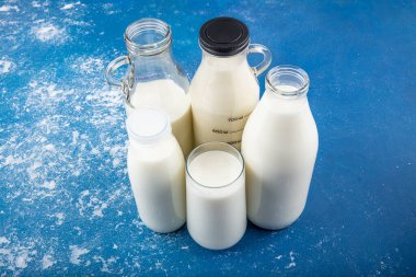 Temiz kavanozlardaki saf süt içecekleri ve şişeler mavi arka planda doğal olarak sağlıklı gıdalardır. Bir şişe süt ve bir bardak süt mavi arka plandaki ahşap bir masada.. 