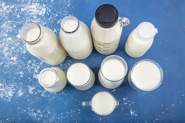 Temiz kavanozlardaki saf süt içecekleri ve şişeler mavi arka planda doğal olarak sağlıklı gıdalardır. Bir şişe süt ve bir bardak süt mavi arka plandaki ahşap bir masada.. 