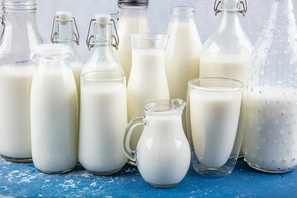 Temiz kavanozlardaki saf süt içecekleri ve şişeler mavi arka planda doğal olarak sağlıklı gıdalardır. Bir şişe süt ve bir bardak süt mavi arka plandaki ahşap bir masada.. 