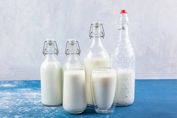 Temiz kavanozlardaki saf süt içecekleri ve şişeler mavi arka planda doğal olarak sağlıklı gıdalardır. Bir şişe süt ve bir bardak süt mavi arka plandaki ahşap bir masada.. 
