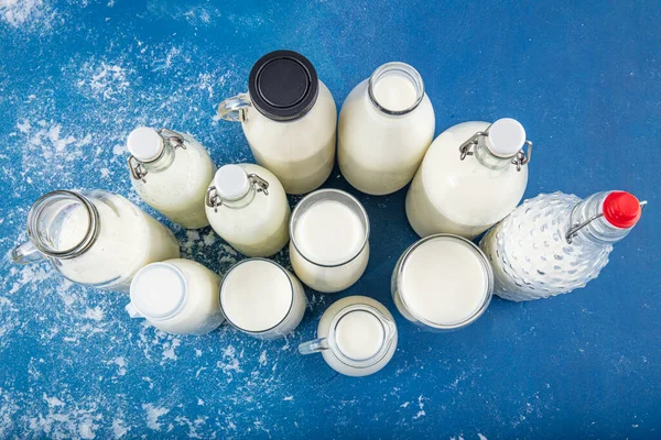 Temiz kavanozlardaki saf süt içecekleri ve şişeler mavi arka planda doğal olarak sağlıklı gıdalardır. Bir şişe süt ve bir bardak süt mavi arka plandaki ahşap bir masada.. 