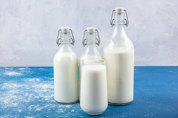 Temiz kavanozlardaki saf süt içecekleri ve şişeler mavi arka planda doğal olarak sağlıklı gıdalardır. Bir şişe süt ve bir bardak süt mavi arka plandaki ahşap bir masada.. 