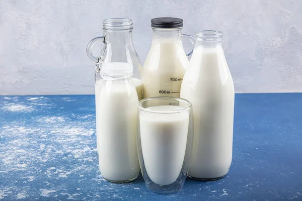 Temiz kavanozlardaki saf süt içecekleri ve şişeler mavi arka planda doğal olarak sağlıklı gıdalardır. Bir şişe süt ve bir bardak süt mavi arka plandaki ahşap bir masada.. 
