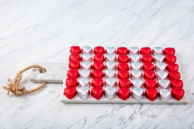 Kırmızı folyoya sarılı kalp şeklinde çikolata şekerler mermer arka planda izole edilmiş. Sevgililer Günü için renkli kalp şeklinde çikolata..