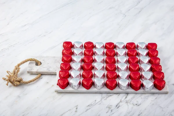 Kırmızı folyoya sarılı kalp şeklinde çikolata şekerler mermer arka planda izole edilmiş. Sevgililer Günü için renkli kalp şeklinde çikolata..