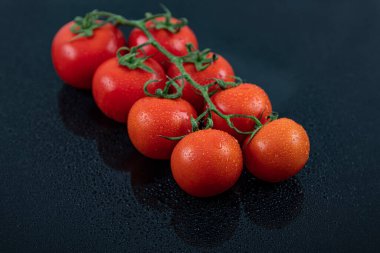 Güzel, taze, sarmaşık domatesleri (kiraz), bir damla su, çiğ, bütün ve yarım. Siyah desenli arka planda. Akdeniz diyetinin içeriği. Kopyalama alanı olan üst görünüm