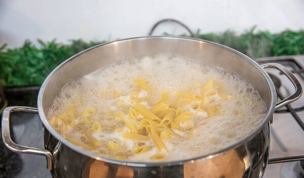 Cooking Pasta pour the penne pasta into a metal pot of boiling water. Boiled penne on a steel colander, in a cooking class.