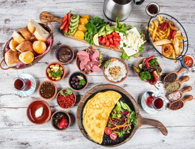 Türk kahvaltı masası. Hamur işleri, sebzeler, yeşiller, zeytinler, peynirler, omlet, baharatlar, reçeller, bal, termosta çay, büyük bir kompozisyon. Restoranda ve kafede kahvaltı konsepti.