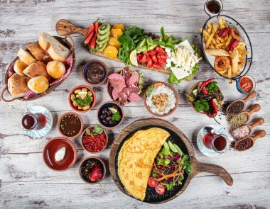Türk kahvaltı masası. Hamur işleri, sebzeler, yeşiller, zeytinler, peynirler, omlet, baharatlar, reçeller, bal, termosta çay, büyük bir kompozisyon. Restoranda ve kafede kahvaltı konsepti.