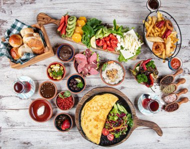 Türk kahvaltı masası. Hamur işleri, sebzeler, yeşiller, zeytinler, peynirler, omlet, baharatlar, reçeller, bal, termosta çay, büyük bir kompozisyon. Restoranda ve kafede kahvaltı konsepti.