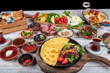 Türk kahvaltı masası. Hamur işleri, sebzeler, yeşiller, zeytinler, peynirler, omlet, baharatlar, reçeller, bal, termosta çay, büyük bir kompozisyon. Restoranda ve kafede kahvaltı konsepti.