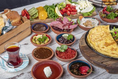 Türk kahvaltı masası. Hamur işleri, sebzeler, yeşiller, zeytinler, peynirler, omlet, baharatlar, reçeller, bal, termosta çay, büyük bir kompozisyon. Restoranda ve kafede kahvaltı konsepti.