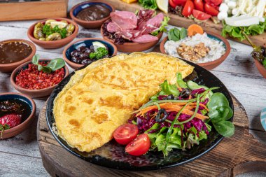 Türk kahvaltı masası. Hamur işleri, sebzeler, yeşiller, zeytinler, peynirler, omlet, baharatlar, reçeller, bal, termosta çay, büyük bir kompozisyon. Restoranda ve kafede kahvaltı konsepti.