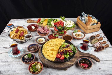 Türk kahvaltı masası. Hamur işleri, sebzeler, yeşiller, zeytinler, peynirler, omlet, baharatlar, reçeller, bal, termosta çay, büyük bir kompozisyon. Restoranda ve kafede kahvaltı konsepti.
