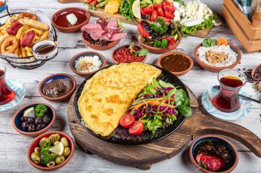 Türk kahvaltı masası. Hamur işleri, sebzeler, yeşiller, zeytinler, peynirler, omlet, baharatlar, reçeller, bal, termosta çay, büyük bir kompozisyon. Restoranda ve kafede kahvaltı konsepti.