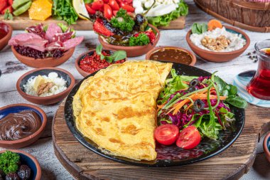 Türk kahvaltı masası. Hamur işleri, sebzeler, yeşiller, zeytinler, peynirler, omlet, baharatlar, reçeller, bal, termosta çay, büyük bir kompozisyon. Restoranda ve kafede kahvaltı konsepti.
