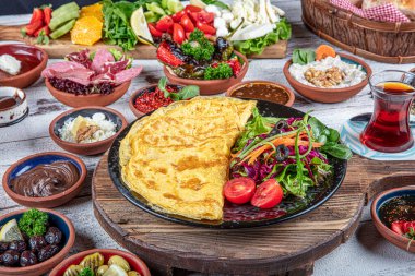 Türk kahvaltı masası. Hamur işleri, sebzeler, yeşiller, zeytinler, peynirler, omlet, baharatlar, reçeller, bal, termosta çay, büyük bir kompozisyon. Restoranda ve kafede kahvaltı konsepti.