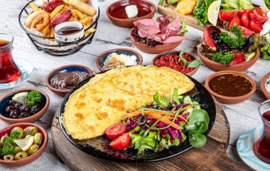 Türk kahvaltı masası. Hamur işleri, sebzeler, yeşiller, zeytinler, peynirler, omlet, baharatlar, reçeller, bal, termosta çay, büyük bir kompozisyon. Restoranda ve kafede kahvaltı konsepti.
