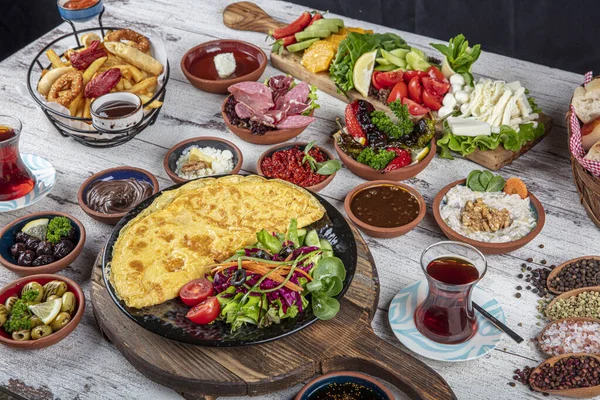 Türk kahvaltı masası. Hamur işleri, sebzeler, yeşiller, zeytinler, peynirler, omlet, baharatlar, reçeller, bal, termosta çay, büyük bir kompozisyon. Restoranda ve kafede kahvaltı konsepti.