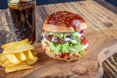 Lezzetli ve iştah açıcı burger, domates, marul, salatalık, eritilmiş peynir ve soğanlı Brioche ekmeği, ahşap bir tahtada patates kızartmasıyla servis edilir.