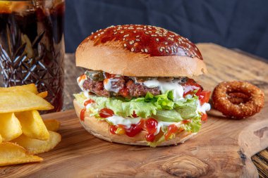 Lezzetli ve iştah açıcı burger, domates, marul, salatalık, eritilmiş peynir ve soğanlı Brioche ekmeği, ahşap bir tahtada patates kızartmasıyla servis edilir.
