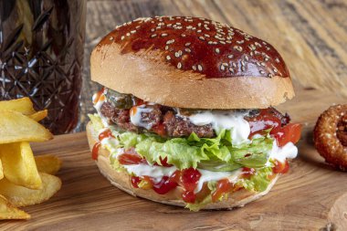 Lezzetli ve iştah açıcı burger, domates, marul, salatalık, eritilmiş peynir ve soğanlı Brioche ekmeği, ahşap bir tahtada patates kızartmasıyla servis edilir.