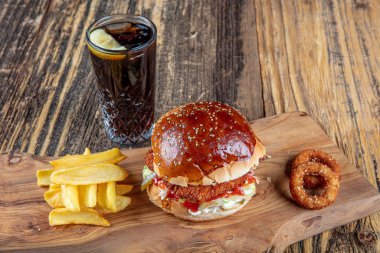 Lezzetli ve iştah açıcı burger, domates, marul, salatalık, eritilmiş peynir ve soğanlı Brioche ekmeği, ahşap bir tahtada patates kızartmasıyla servis edilir.