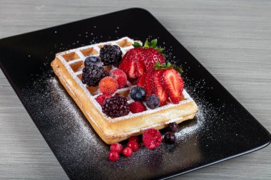 Traditional Belgian waffles with ice cream and berry fruit sauce on plate, selective focus and free space. Macro shot of waffles with, blueberries , blackberries and caramel.