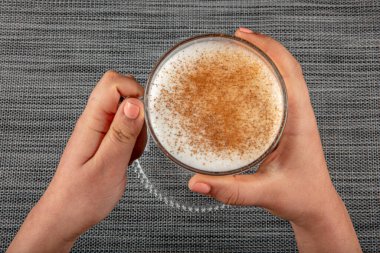 A woman's hand is holding a white cup of hot milk drink with cinnamon called Turkish salep (sahlep).