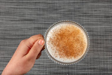 A woman's hand is holding a white cup of hot milk drink with cinnamon called Turkish salep (sahlep).
