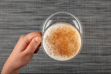A woman's hand is holding a white cup of hot milk drink with cinnamon called Turkish salep (sahlep).