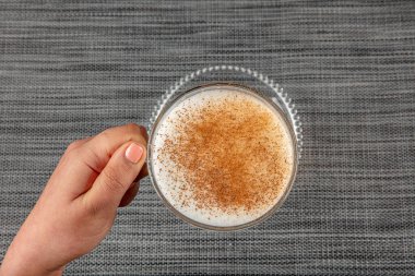 A woman's hand is holding a white cup of hot milk drink with cinnamon called Turkish salep (sahlep).