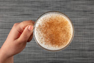A woman's hand is holding a white cup of hot milk drink with cinnamon called Turkish salep (sahlep).