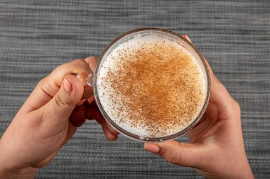 A woman's hand is holding a white cup of hot milk drink with cinnamon called Turkish salep (sahlep).