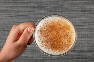 A woman's hand is holding a white cup of hot milk drink with cinnamon called Turkish salep (sahlep).
